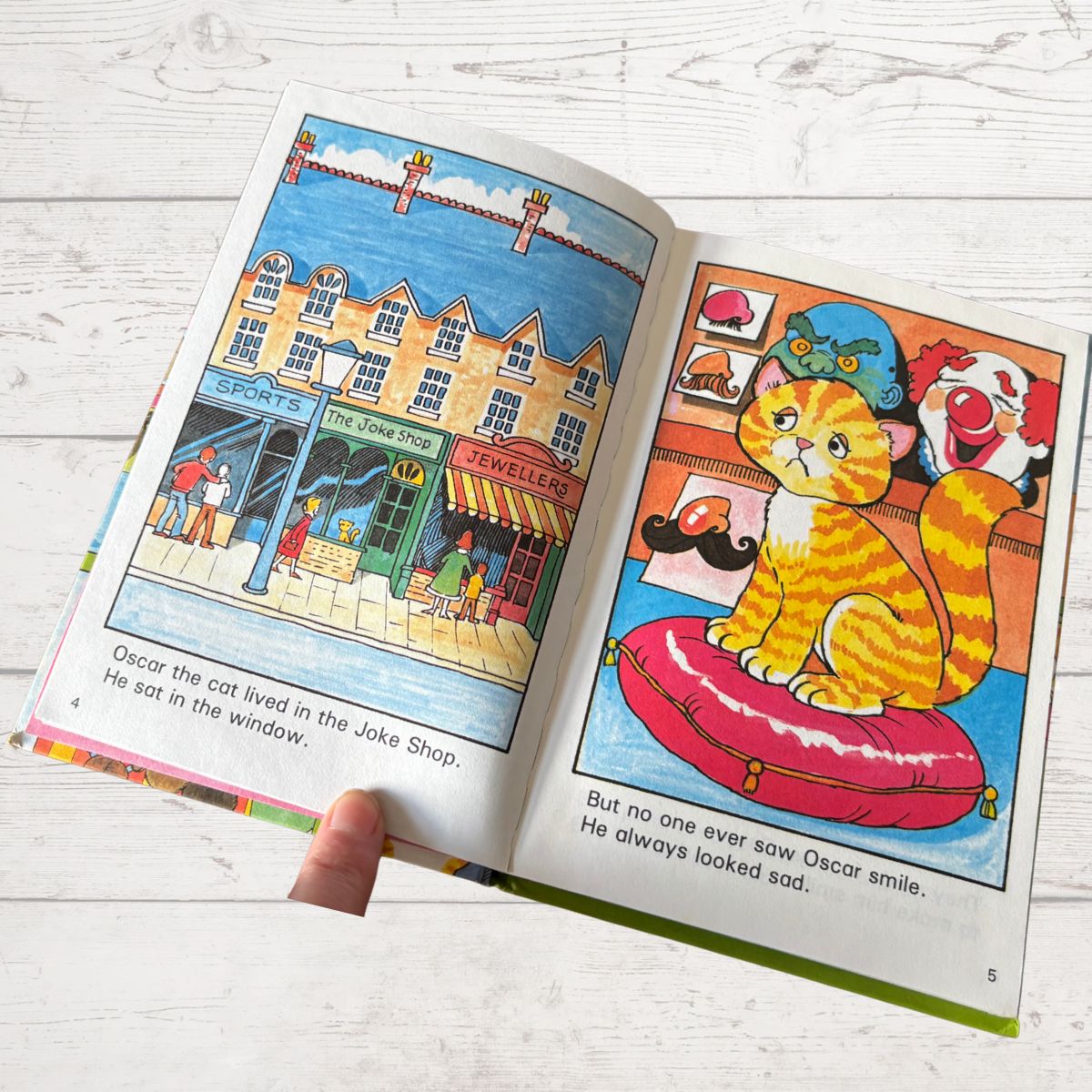 Open children's book with colorful illustrations of a cat and a town scene on a white wooden surface.