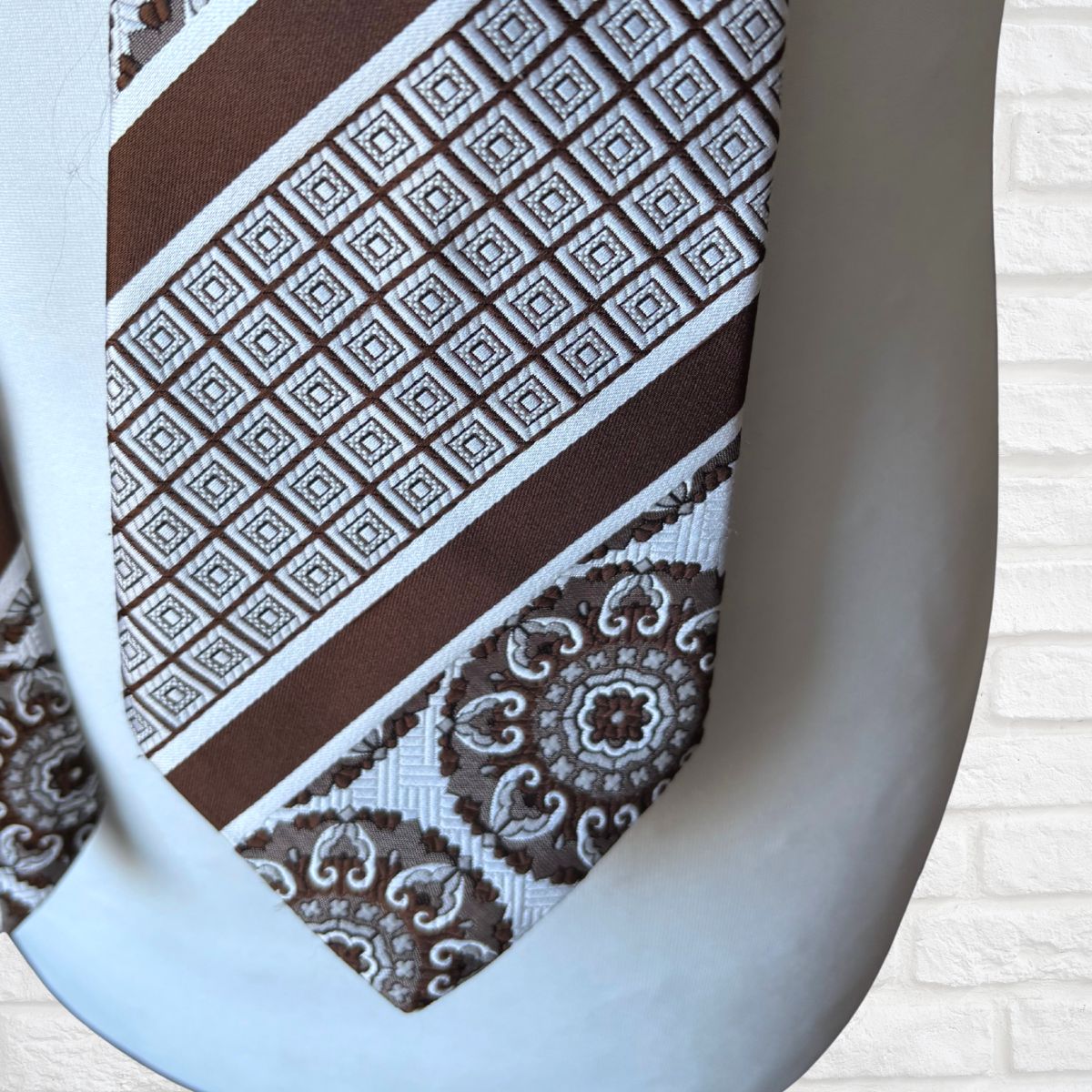 Brown and white patterned tie on a mannequin against a white brick wall.