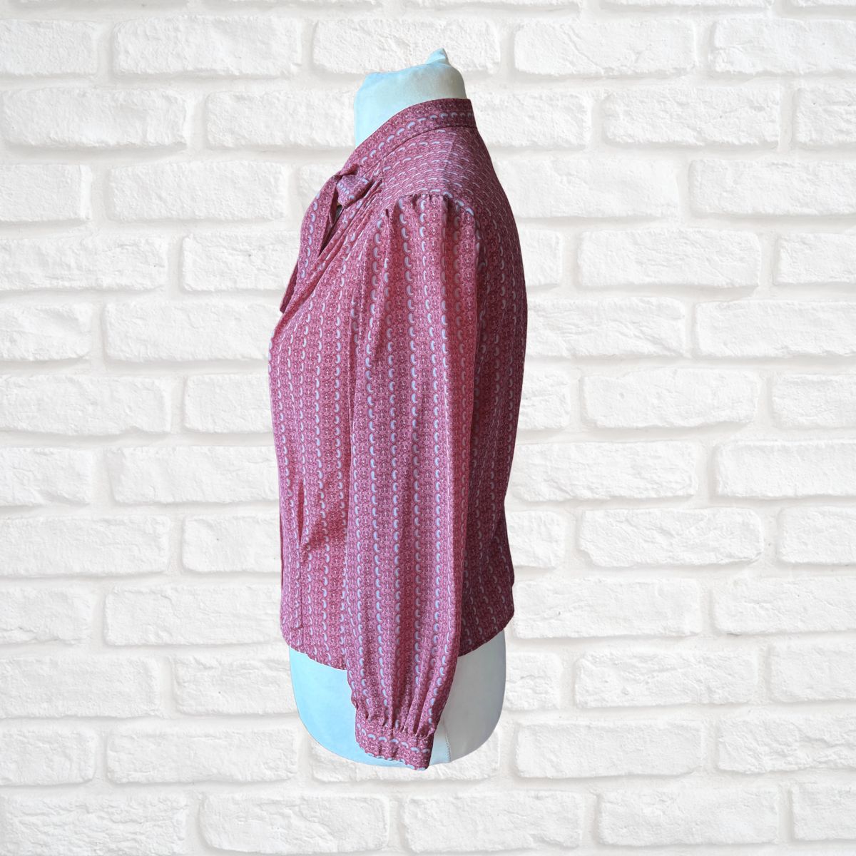 Mannequin wearing a pink patterned blouse against a white brick wall.
