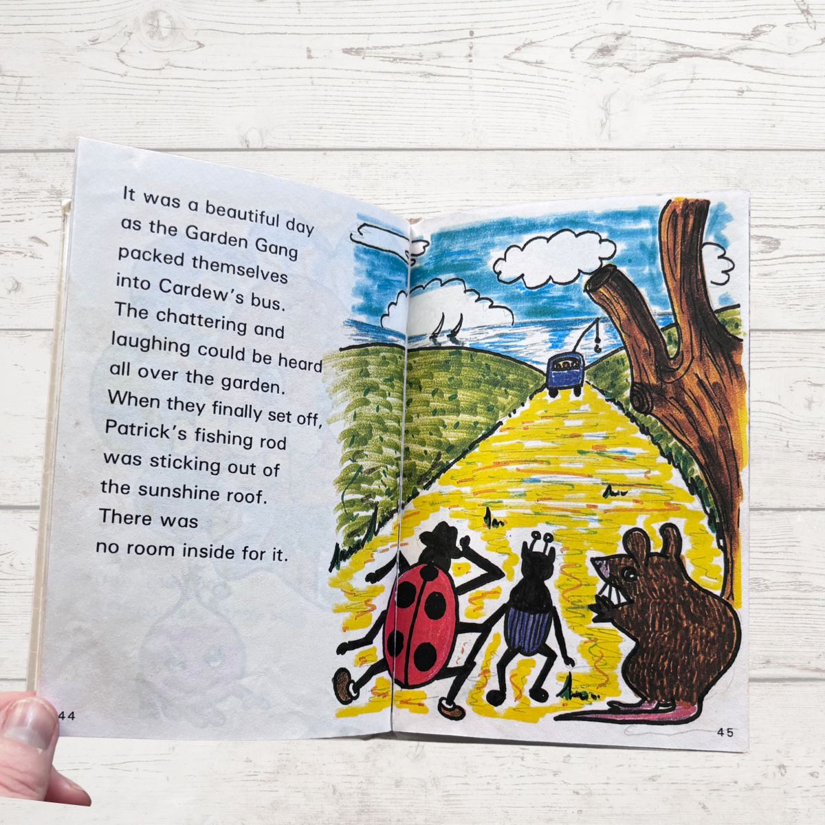 Open book with colorful illustration of animals on a yellow path, held against a light wooden background.
