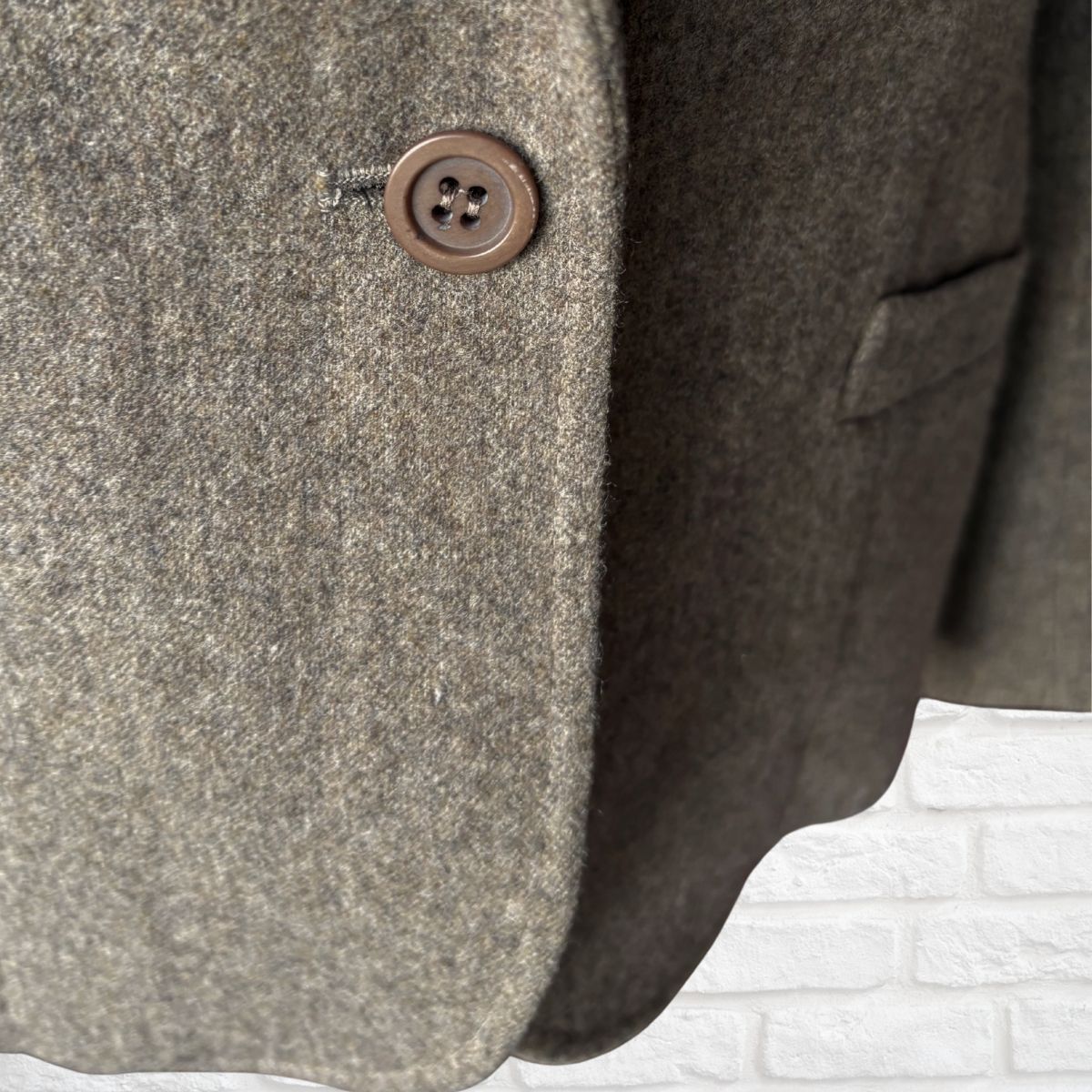 Close-up of a textured gray coat with a brown button on a white brick background