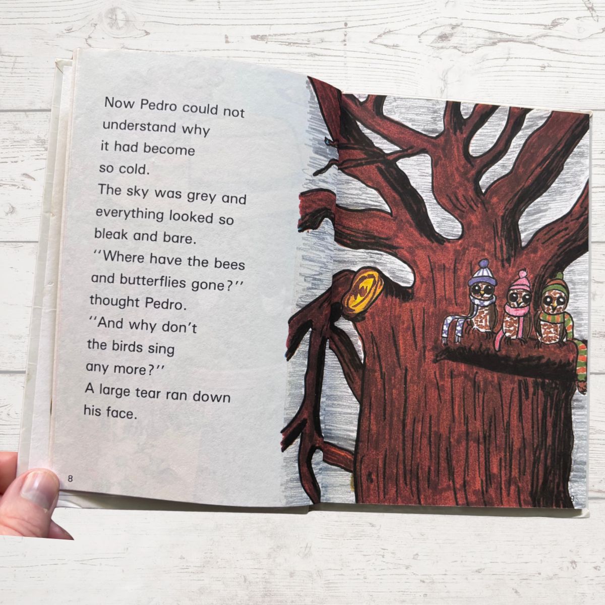 Open book with a illustration of a tree and animals on a white wooden surface