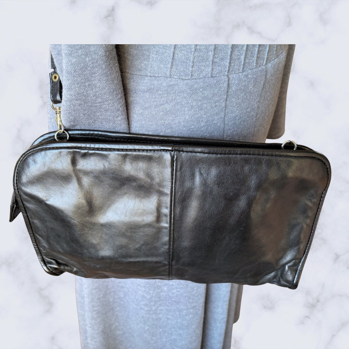 Black leather clutch bag held by a person wearing a gray suit on a light gray background