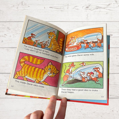 Open book with colorful illustrations of a cat and mice on a wooden surface