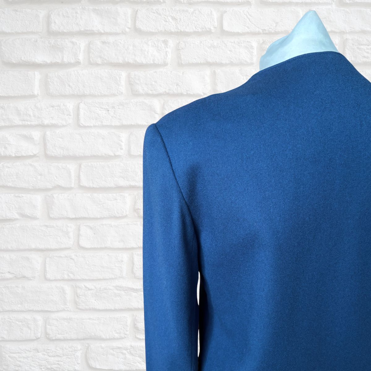 Blue suit jacket on a mannequin against a white brick wall background