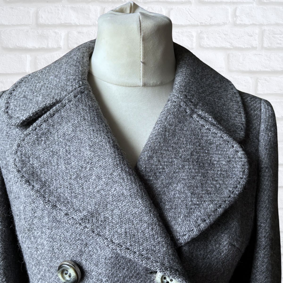Gray coat on a mannequin against a white brick wall background