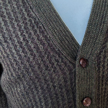 Close-up of a textured green cardigan with brown buttons against a light blue background