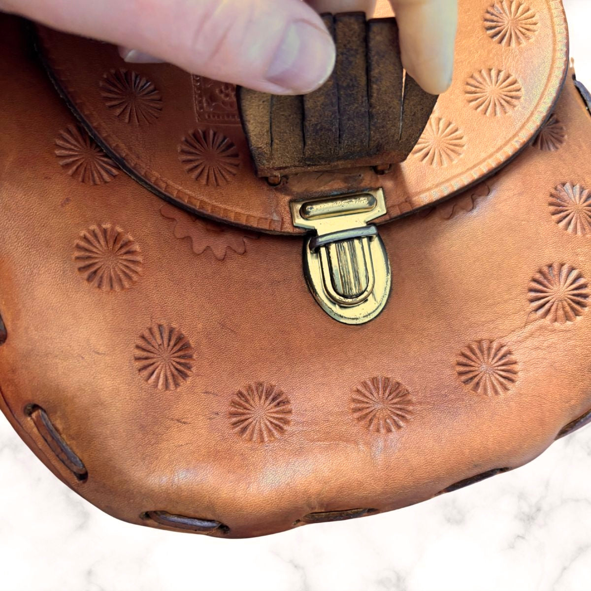 Tooled leather shoulder bag’s  gold metal push button fastening on a white background 