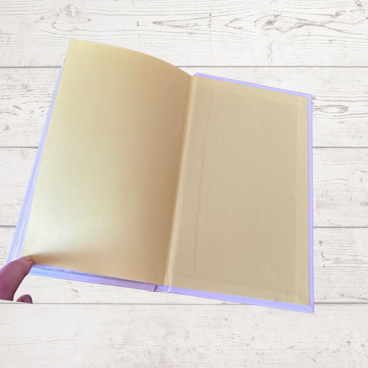 Open beige book held by a hand on a light wooden surface