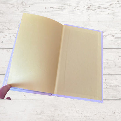 Open beige book held by a hand on a light wooden surface