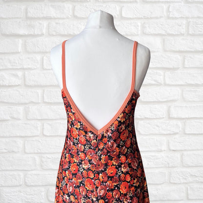 Floral dress with orange straps on a mannequin against a white brick wall.