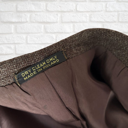Brown fabric with a label indicating 'Dry Clean Only, Made in Poland' against a white brick wall background.