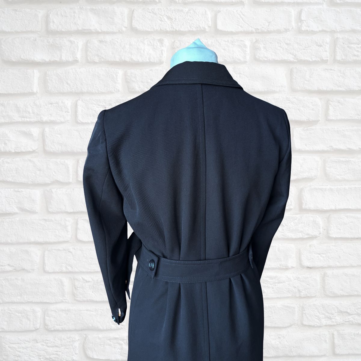 Navy blue coat on a mannequin against a white brick wall background