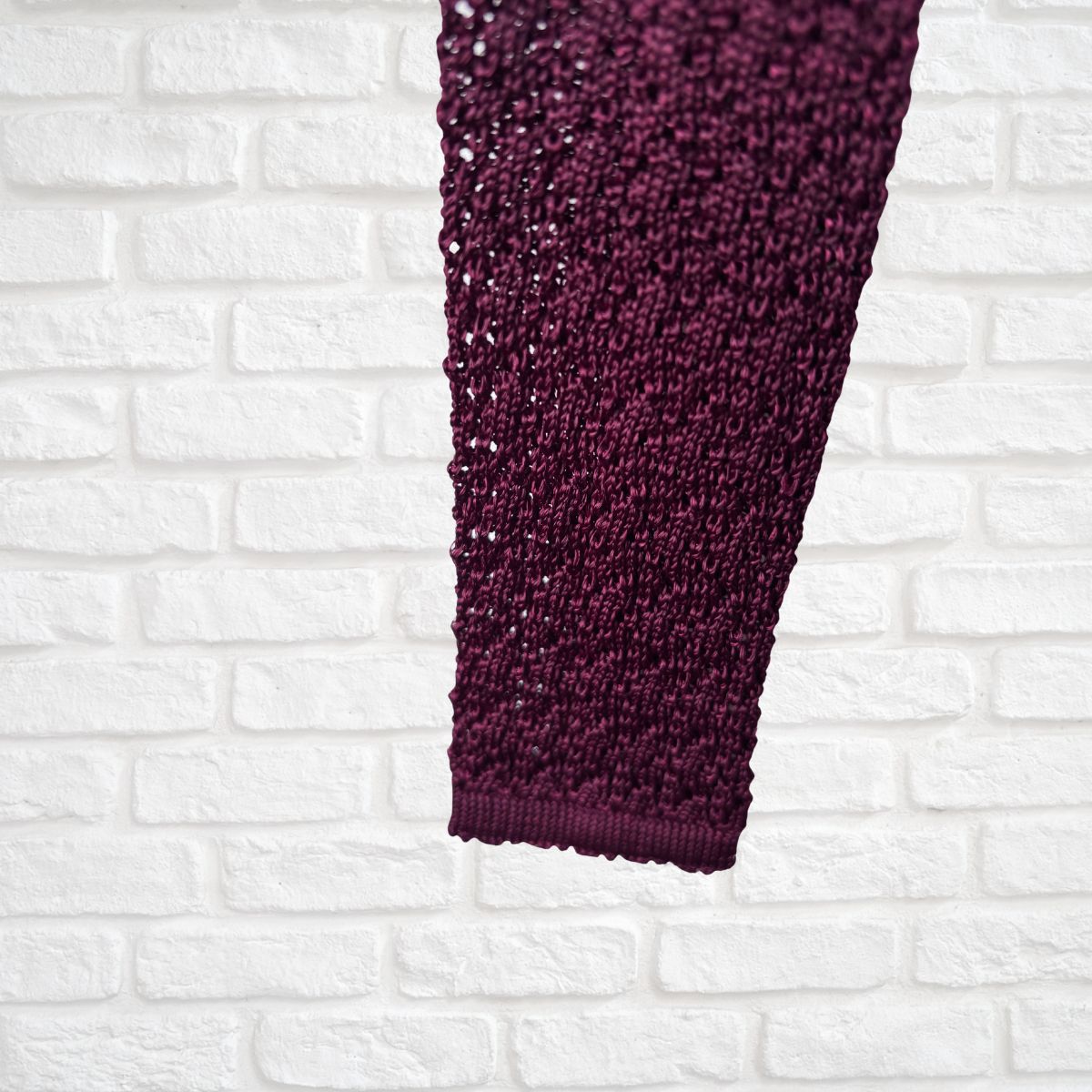 Close-up of a burgundy  textured fabric against a white brick wall background
