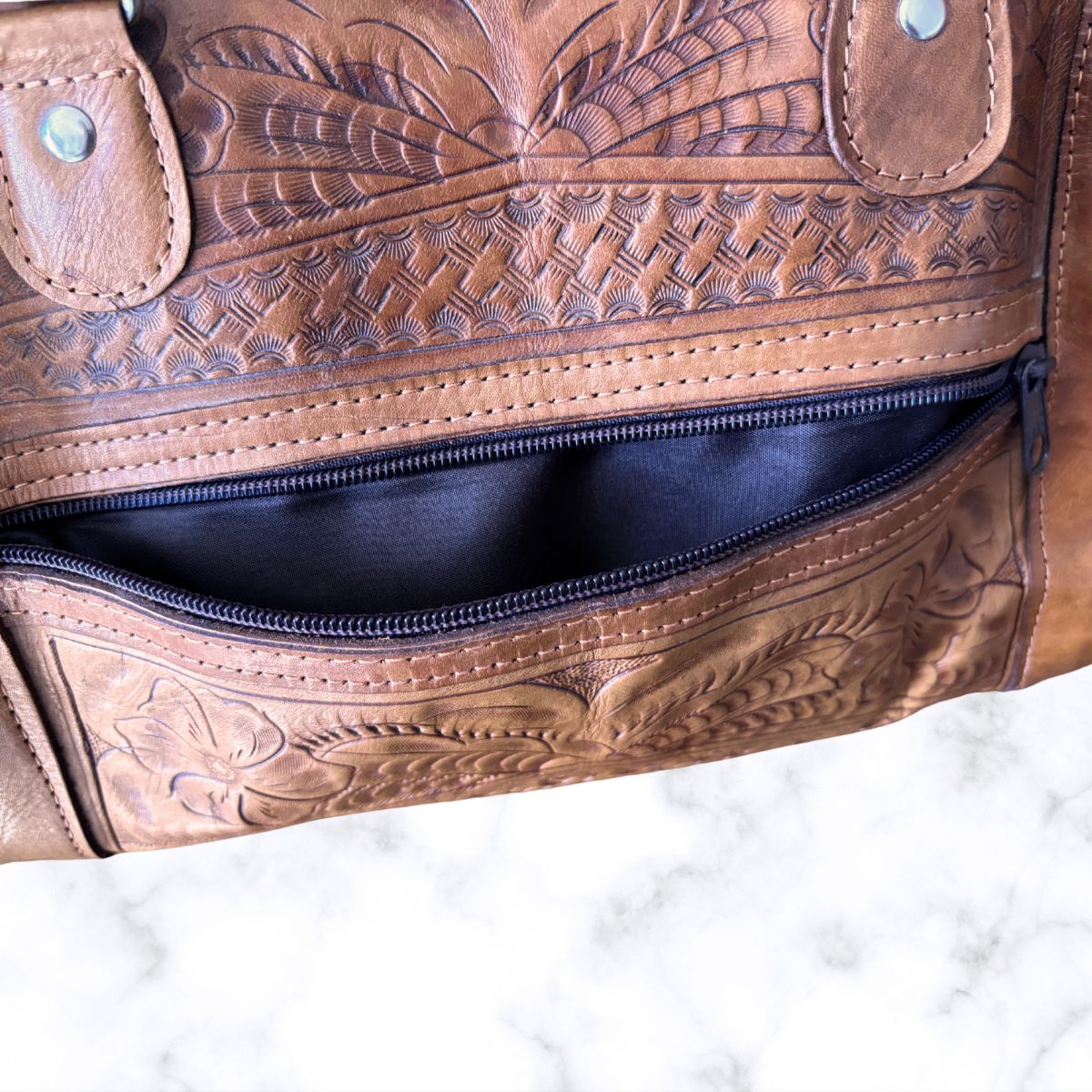 Brown leather bag with intricate embossing on a white background