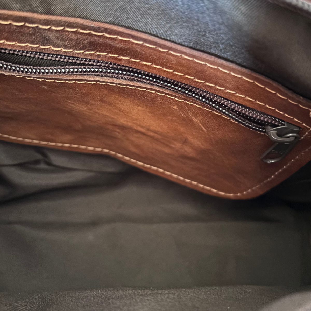 Close-up of a brown leather bag with a zipper on a dark background