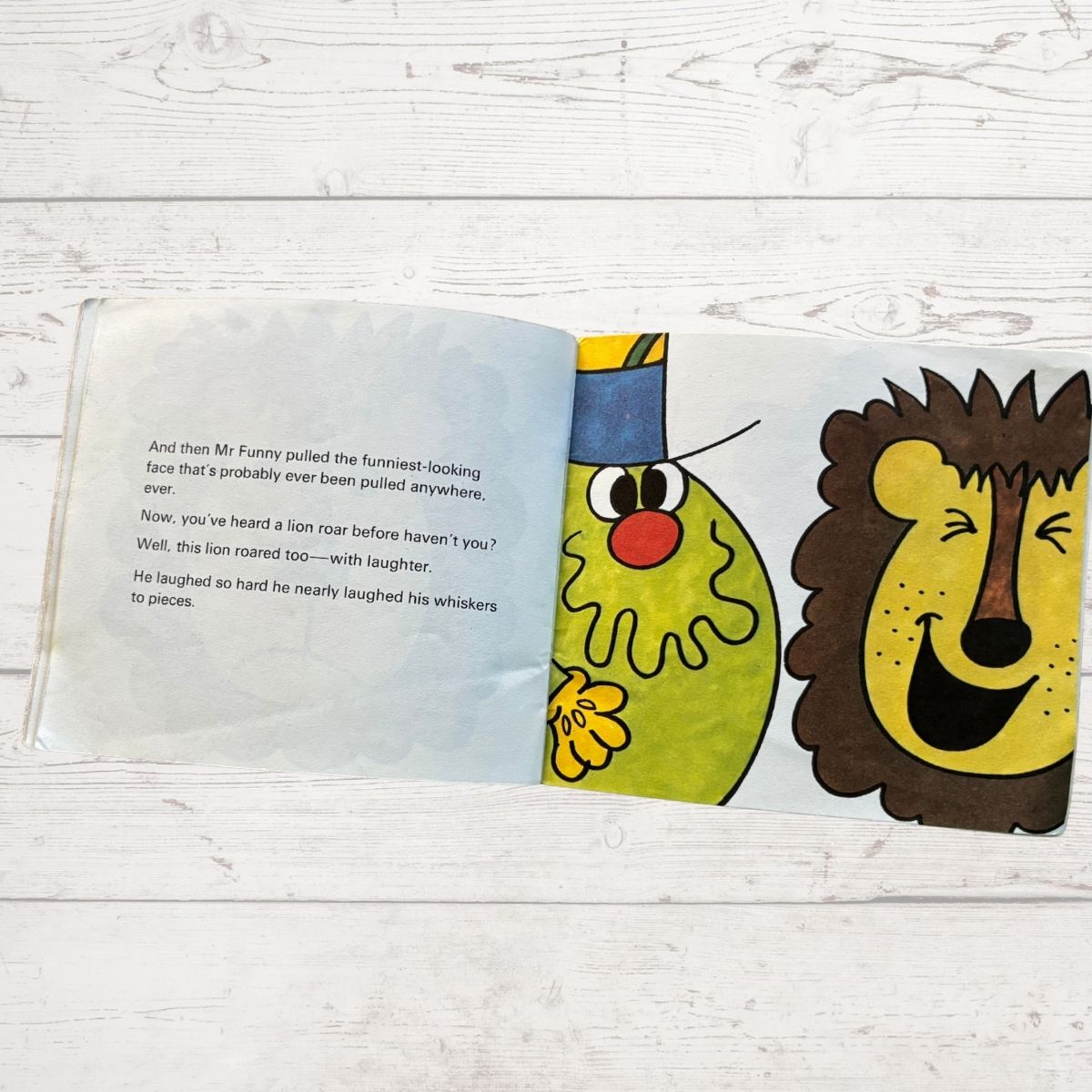 Open book with colorful illustrations of Mr Funny  and a lion on a wooden surface