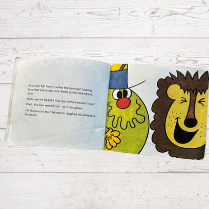 Open book with colorful illustrations of Mr Funny  and a lion on a wooden surface