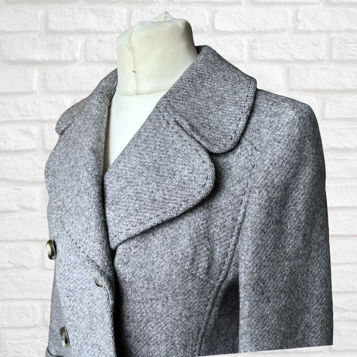 Gray coat on a mannequin against a white brick wall background