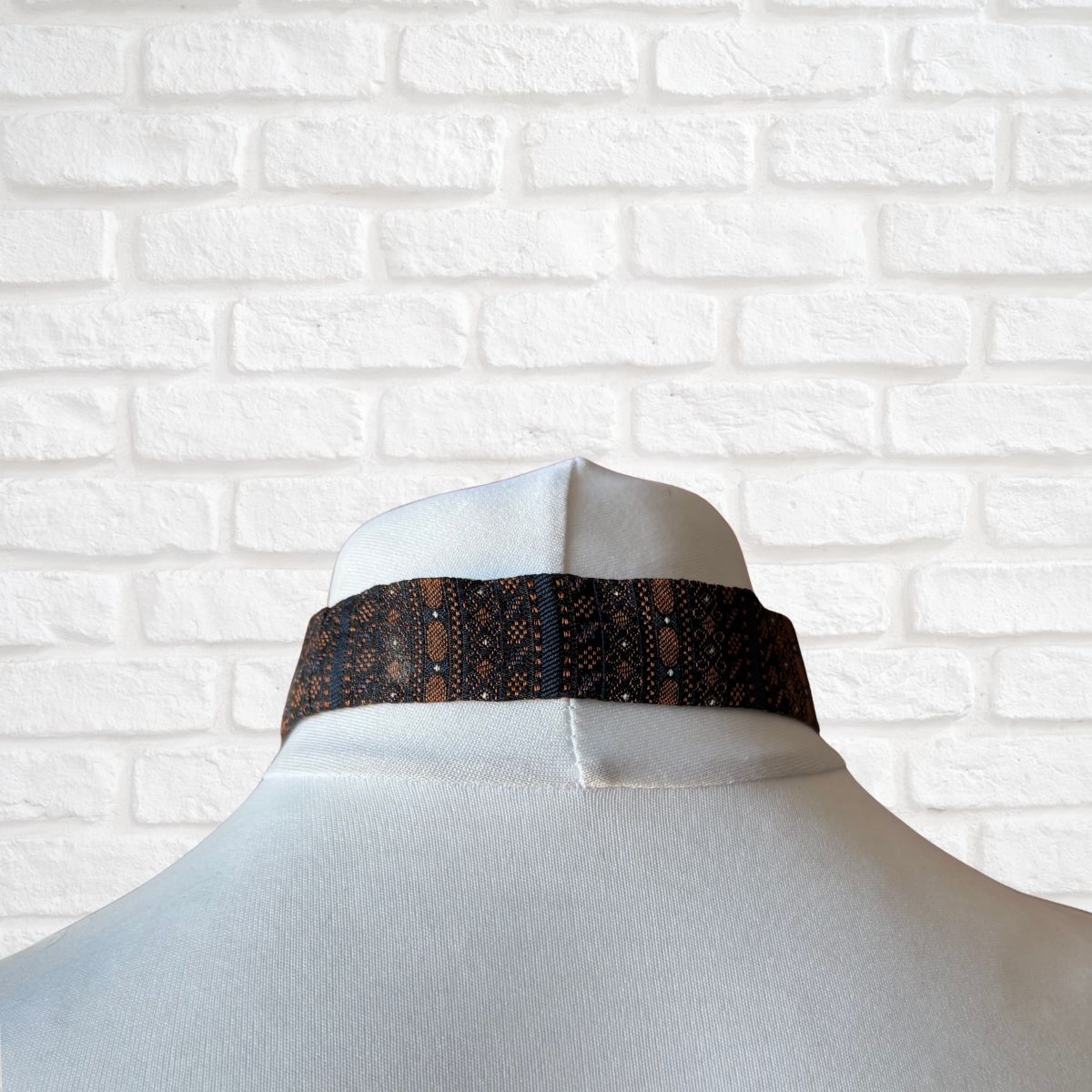 Mannequin with a black and gold patterned tie against a white brick wall.