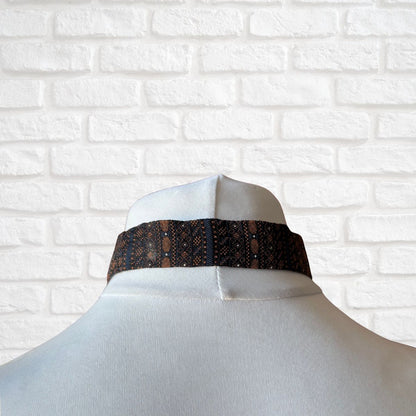 Mannequin with a black and gold patterned tie against a white brick wall.
