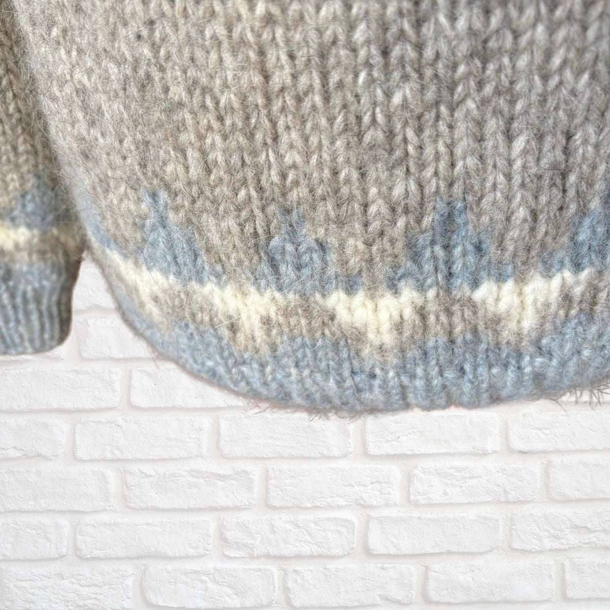 Close-up of a knitted sweater with a textured pattern against a white brick wall.