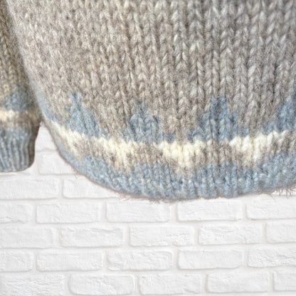Close-up of a knitted sweater with a textured pattern against a white brick wall.