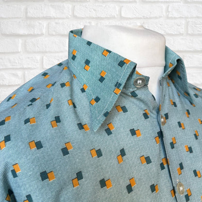 Mannequin wearing a teal shirt with geometric pattern against a white brick wall.
