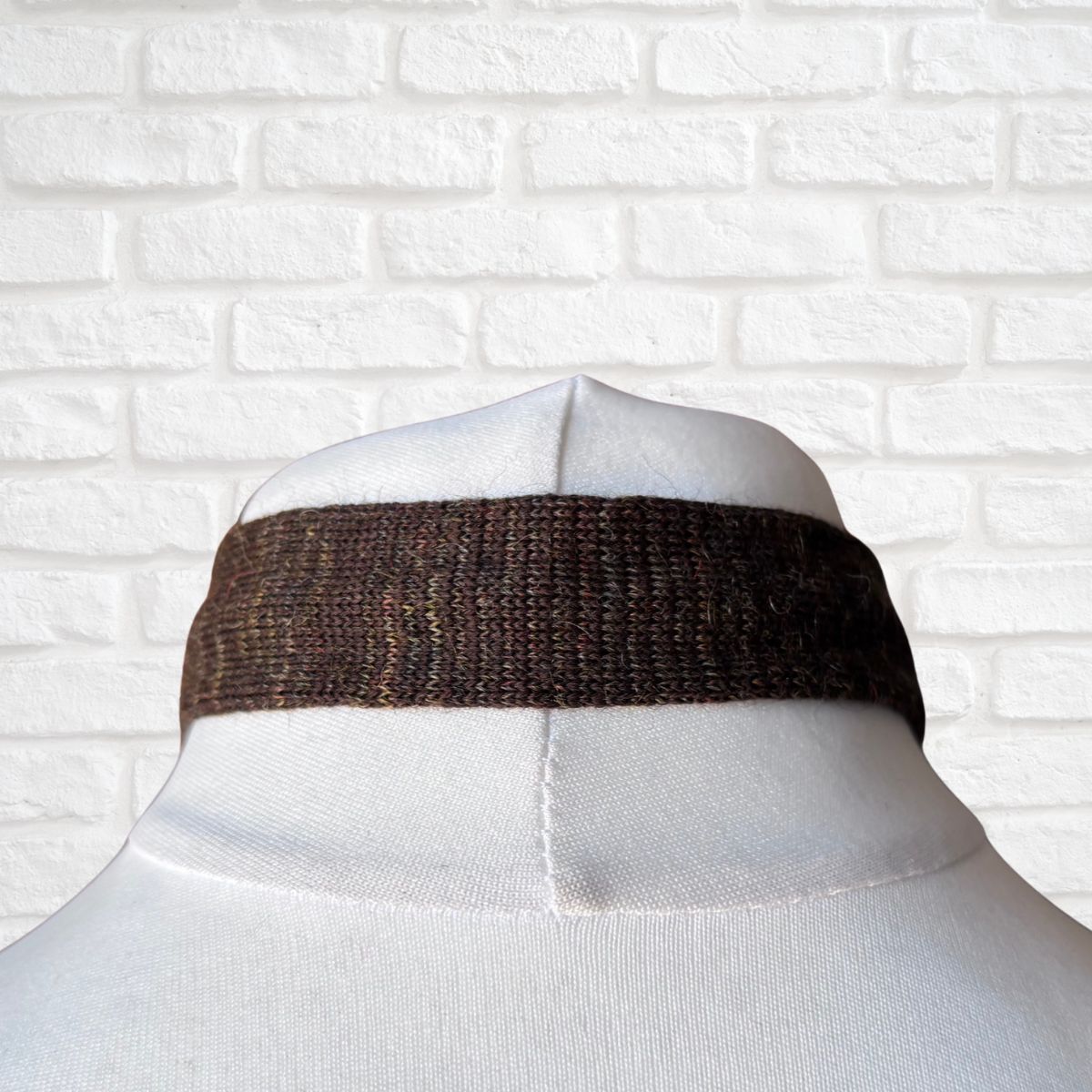 Mannequin wearing a brown tie against a white brick wall.