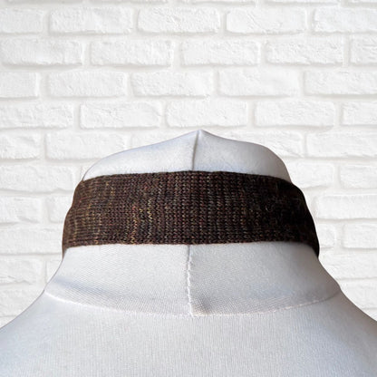 Mannequin wearing a brown tie against a white brick wall.