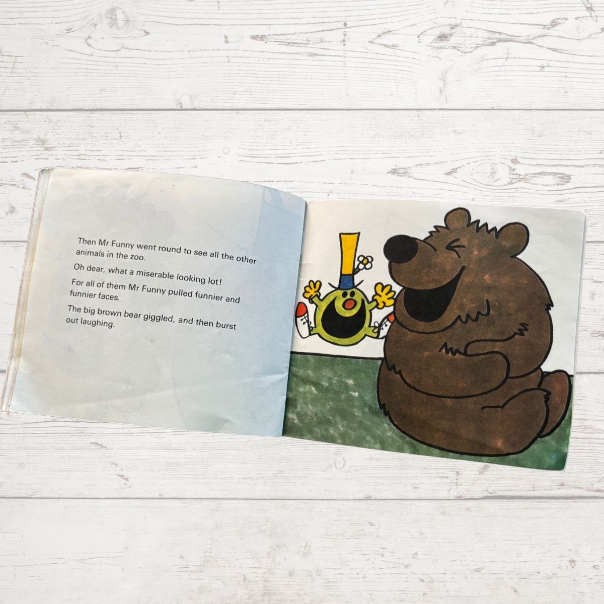 Open children's book with a cartoon bear and other characters on a wooden surface