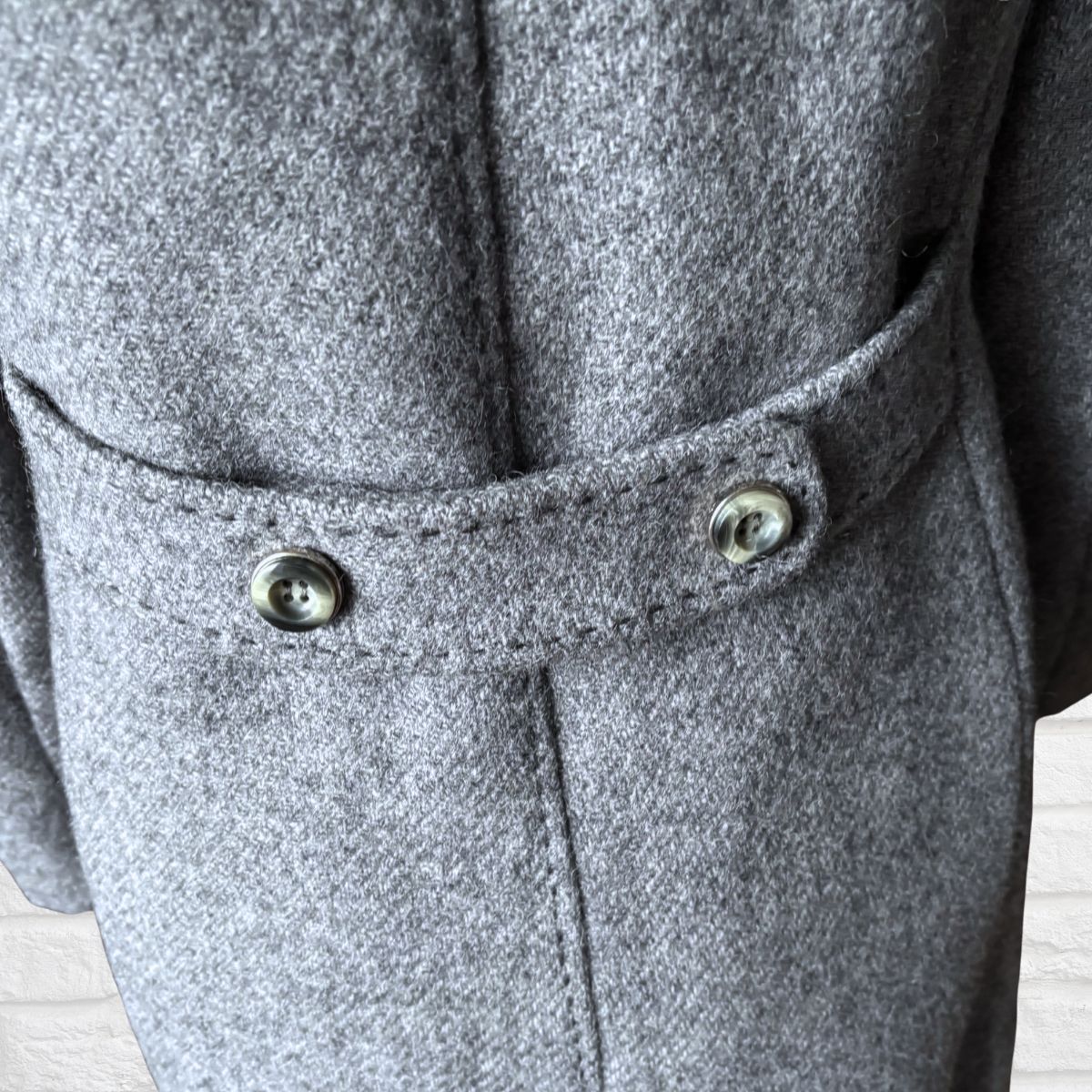Close-up of a gray coat with buttons on a light wooden floor.