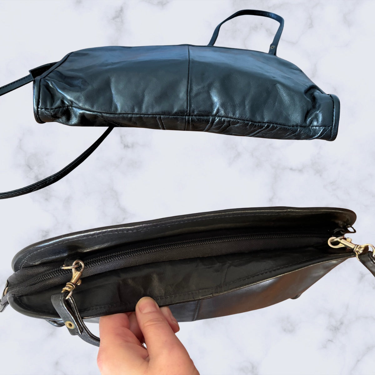 Black leather handbag with gold zipper on a light gray background