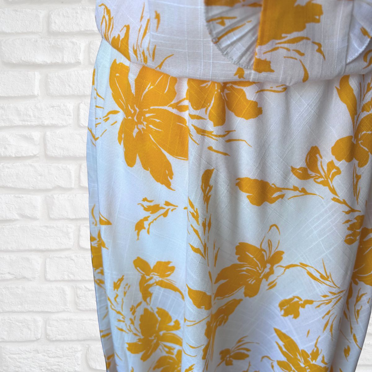 White dress with yellow floral pattern against a white brick wall background