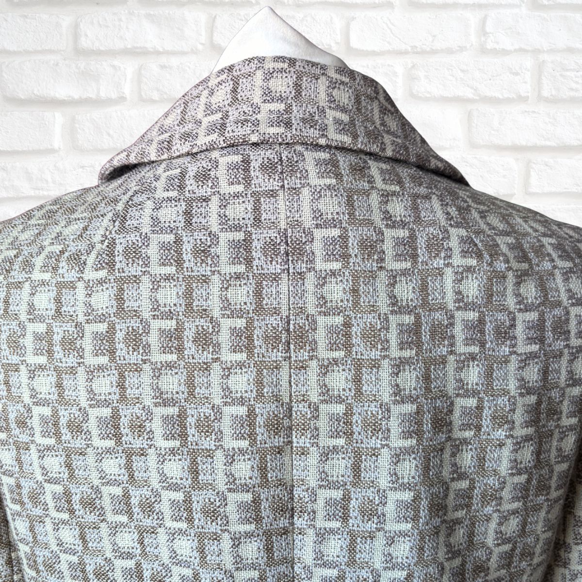 Patterned coat on a mannequin against a white brick wall background