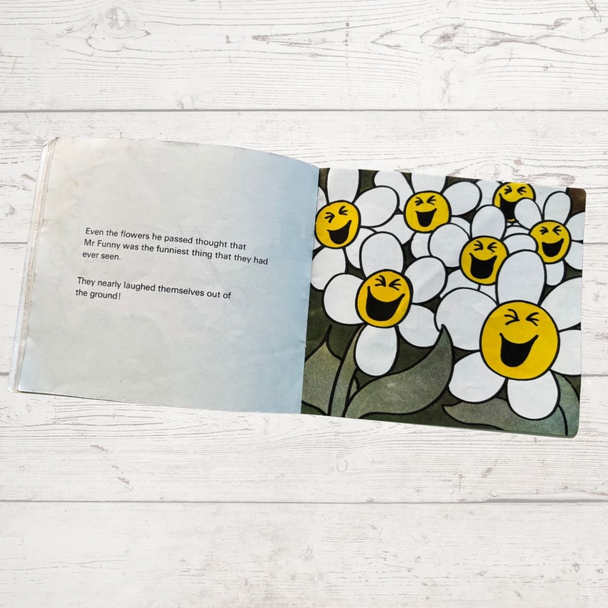 Open book with cartoon flowers laughing on a wooden surface