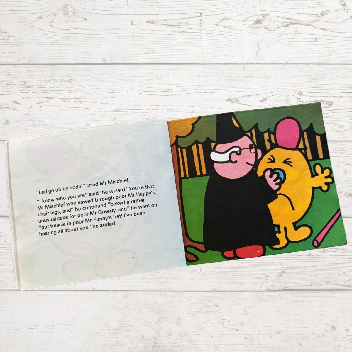 Open book with cartoon illustration of a character in a black robe and a yellow creature on a wooden surface.