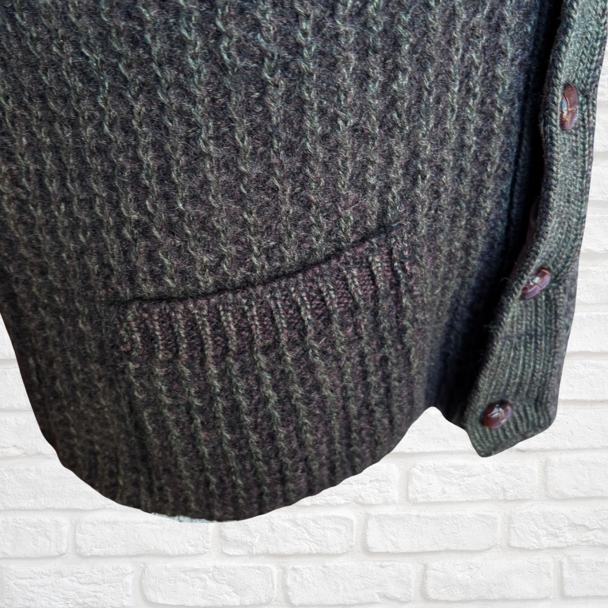 Close-up of a textured brown cardigan on a white brick wall background