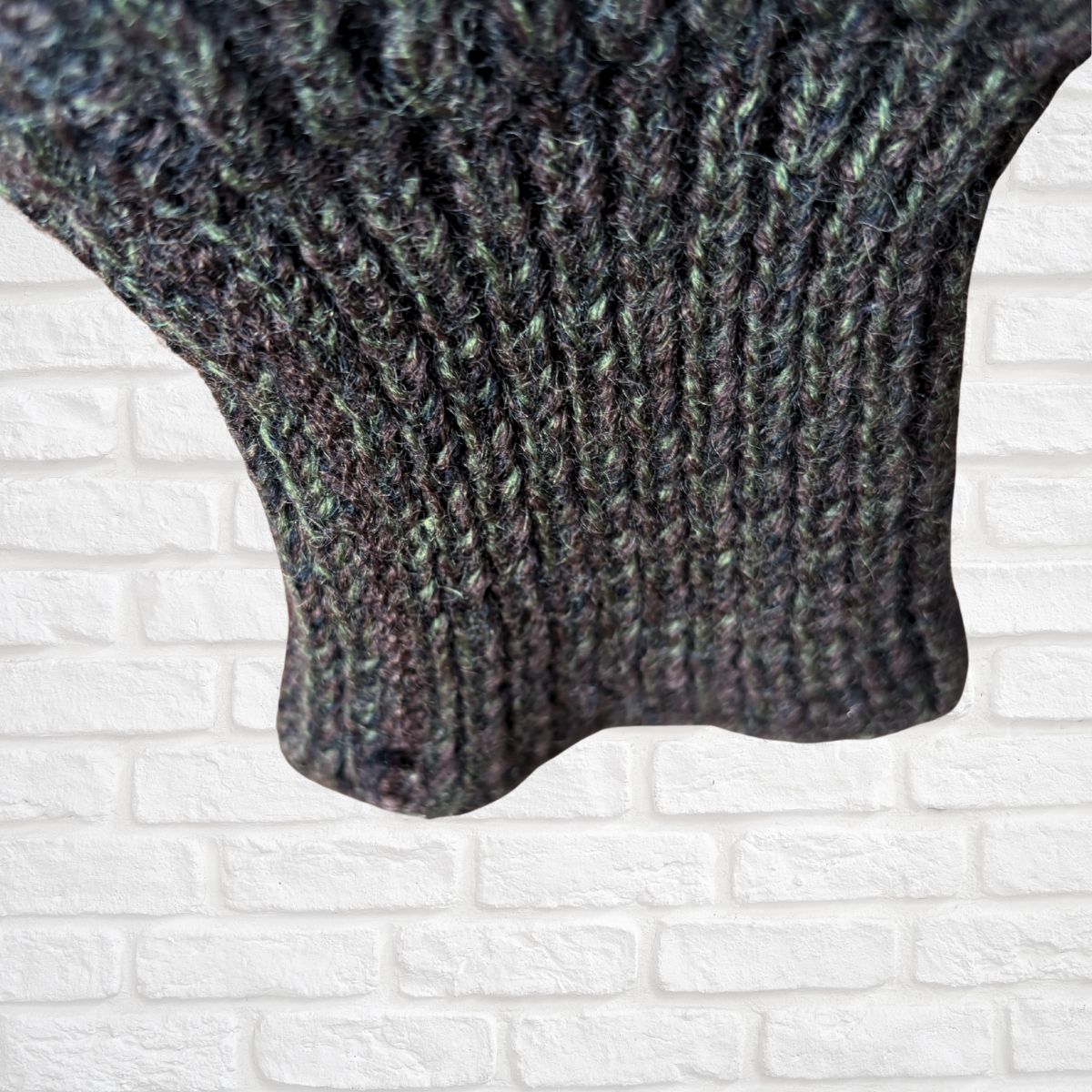 Close-up of a knitted sweater sleeve against a white brick wall background