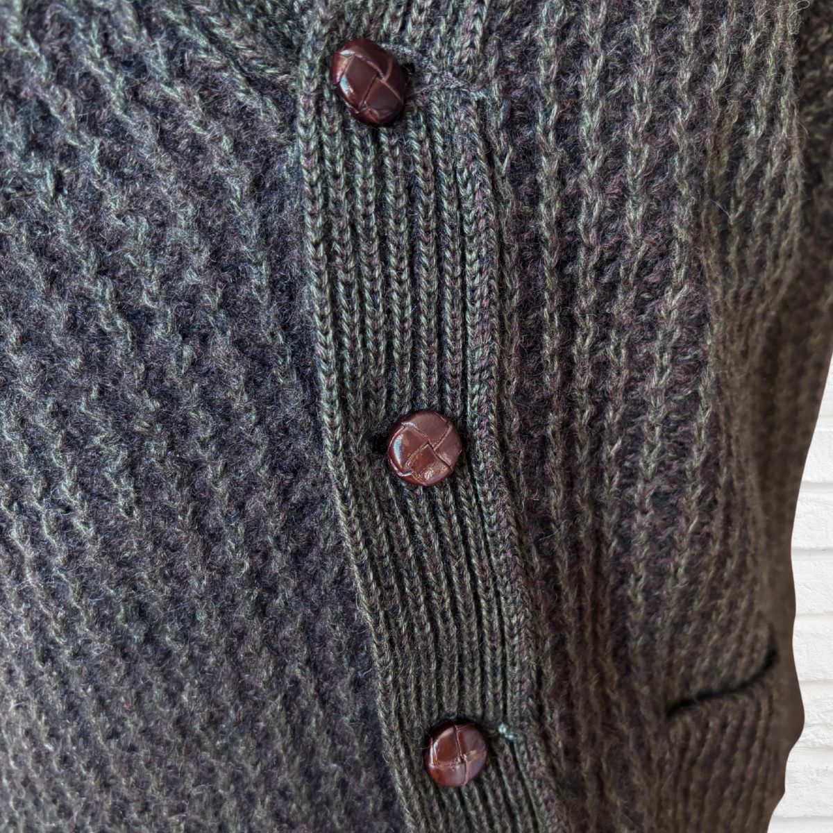 Close-up of a textured cardigan with brown buttons on a neutral background