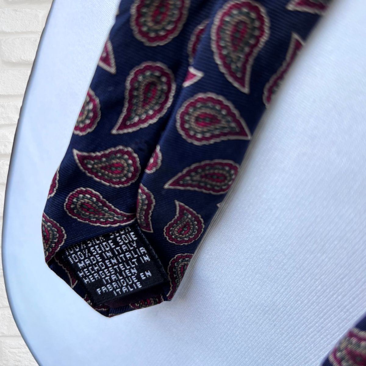 Navy and Red Paisley Silk Vintage Tie On a white brick background - close up 