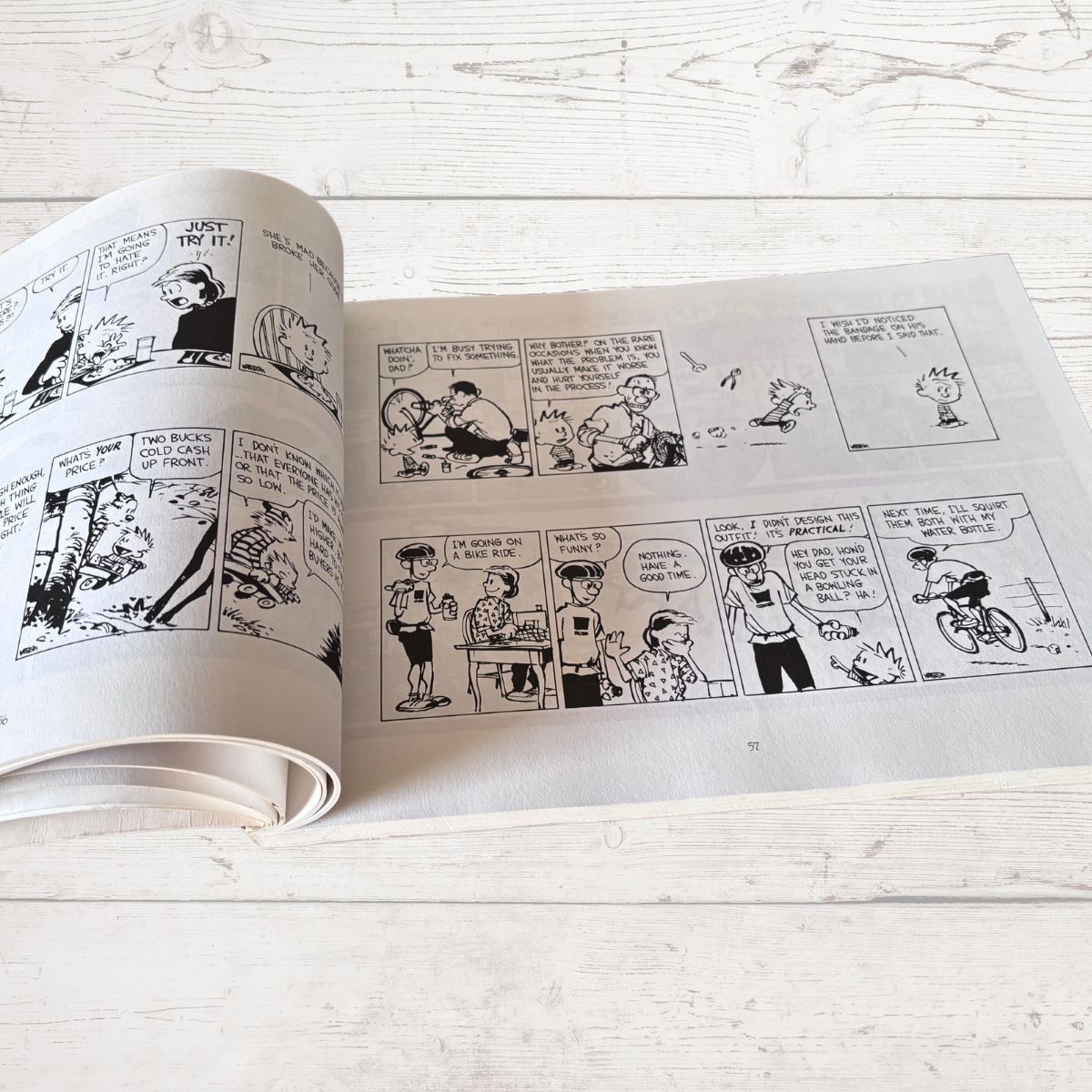 Open comic book with black and white illustrations on a light wooden surface
