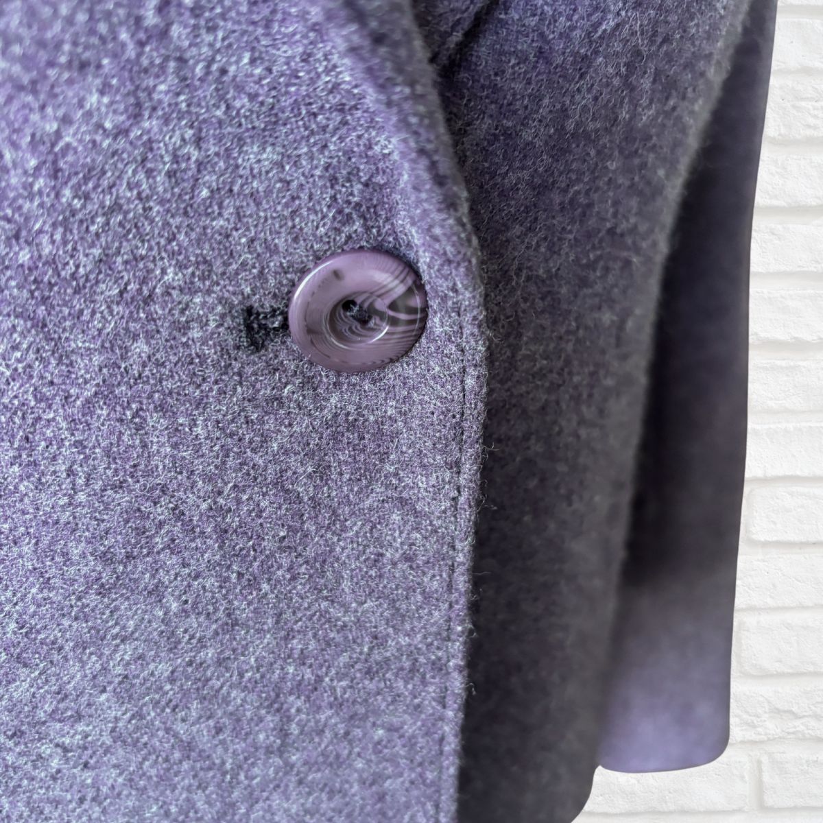 Close-up of a textured purple coat with a button on a light background