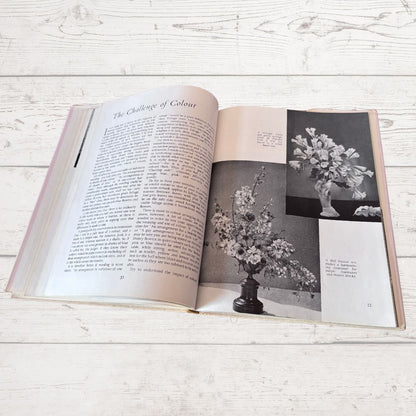 Open book on a wooden surface with text and black and white photos of floral arrangements.
