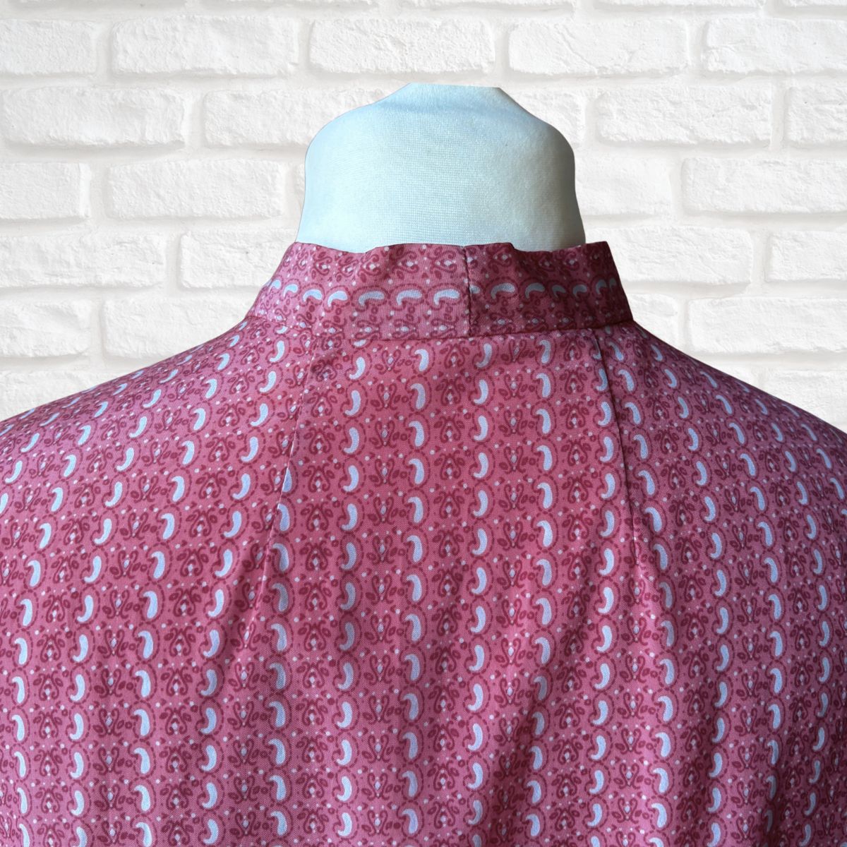 Mannequin wearing a pink and grey patterned shirt against a white brick wall.