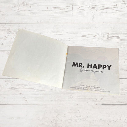 Open book with 'MR. HAPPY' by Roger Hargreaves on a wooden surface