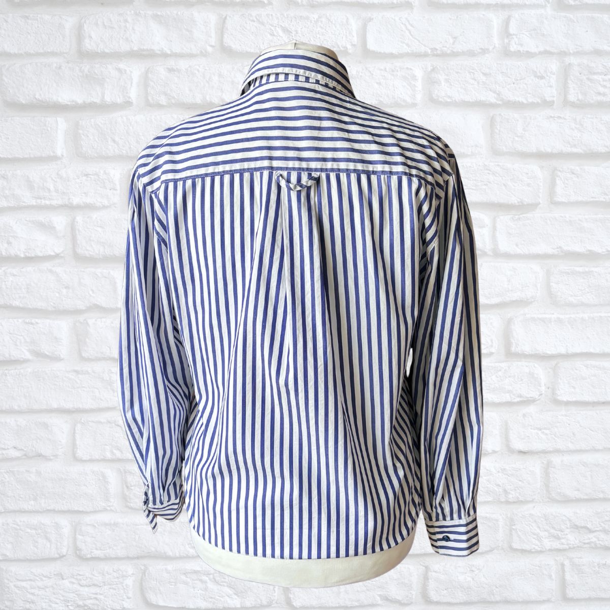 Blue and white striped shirt on a mannequin against a white brick wall.