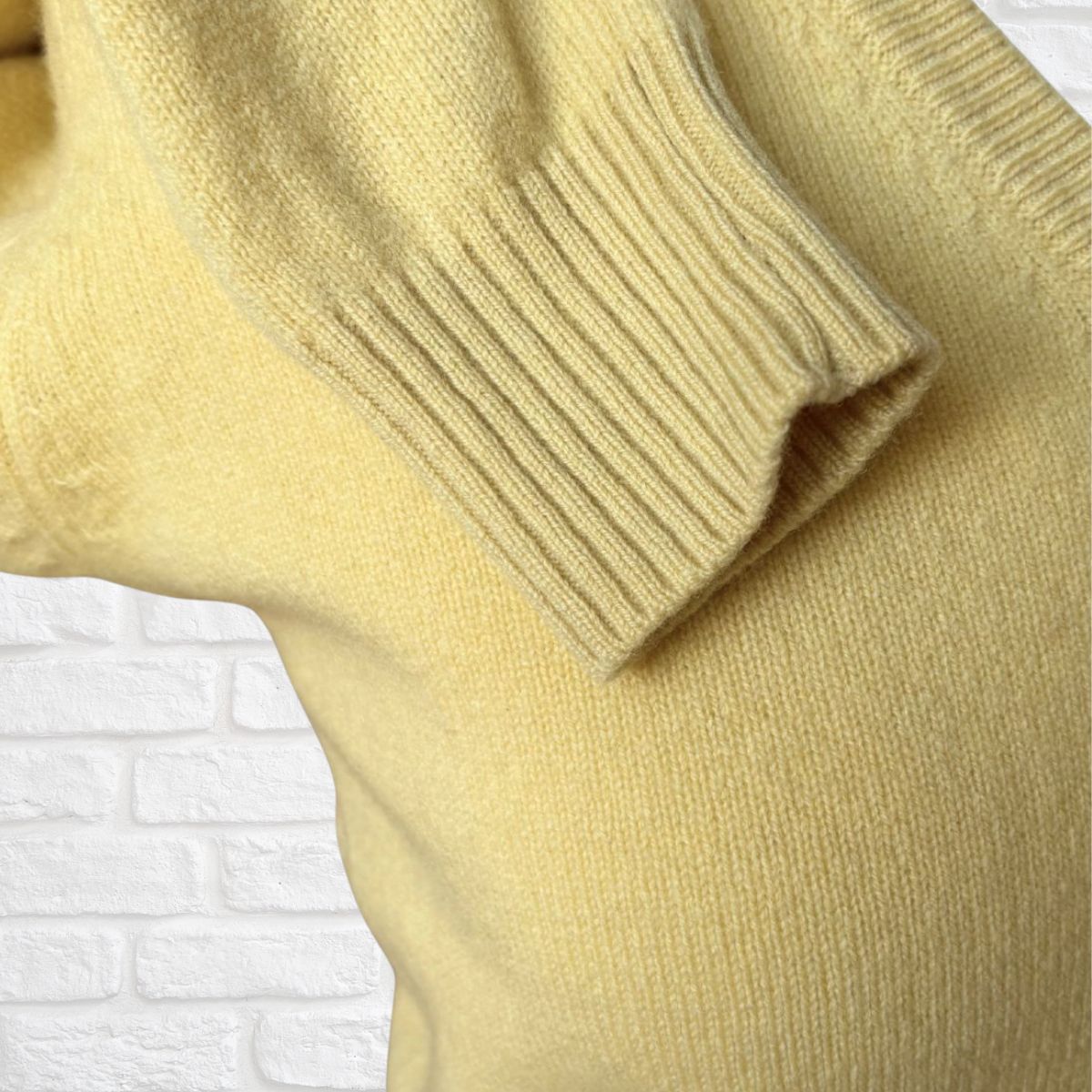 Close-up of a yellow sweater with a textured pattern on a white brick wall background