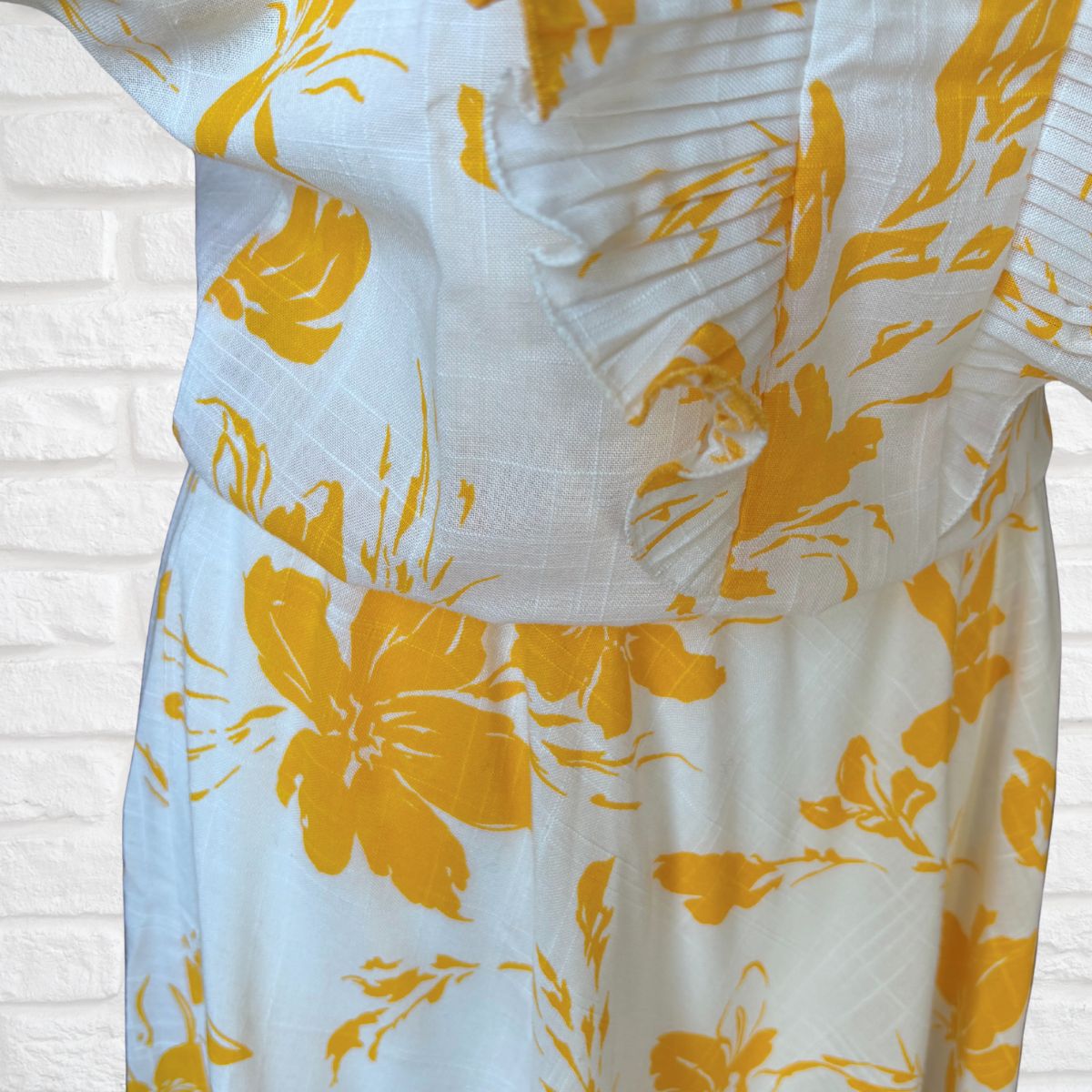 White dress with yellow floral pattern on a white brick wall background