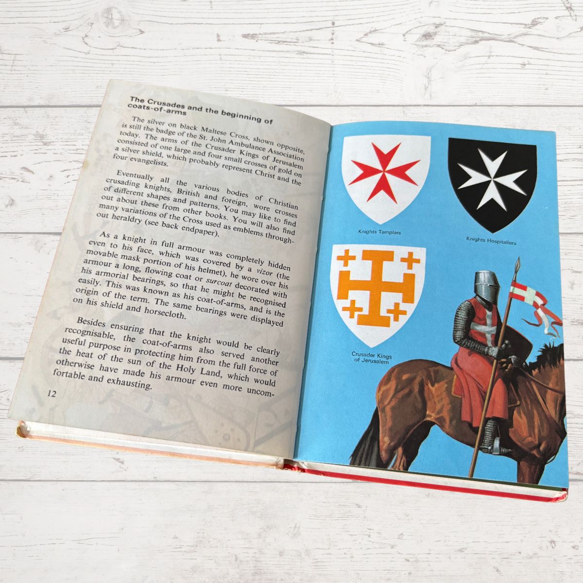 Open book with illustrations of knights and shields on a wooden surface